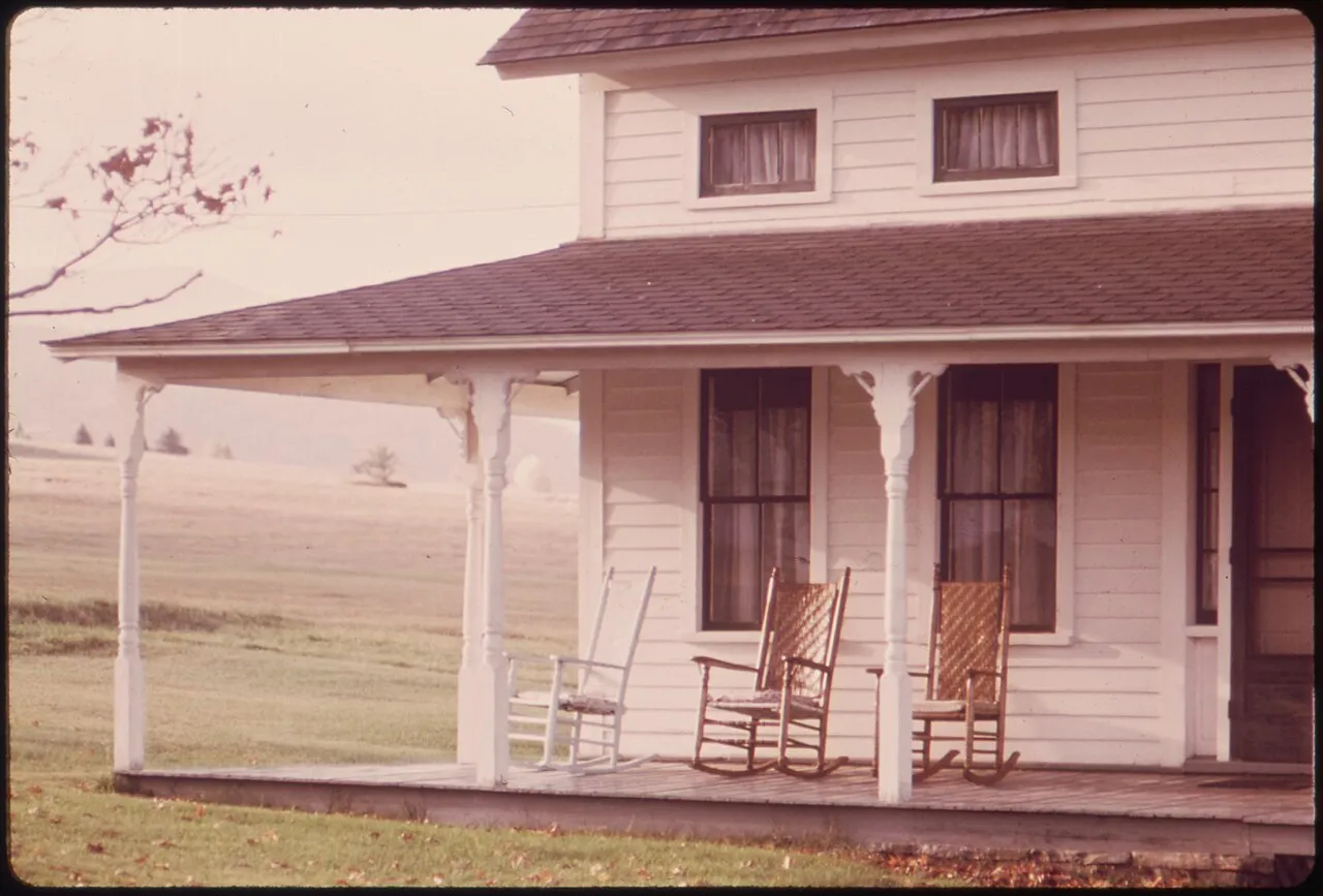 Placeholder stock photo: Rocking chairs on the front porch of an old white farmhouse