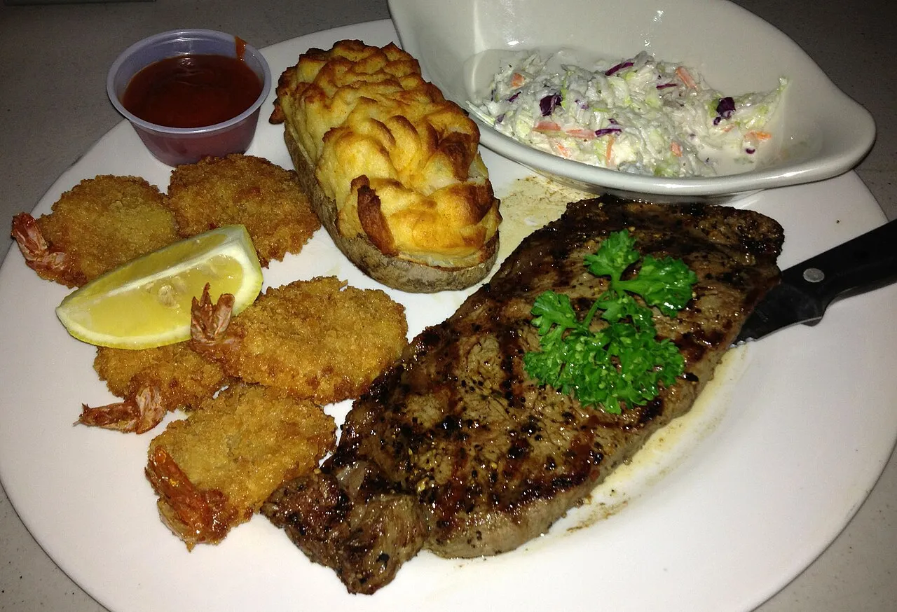 Placeholder stock photo: A grilled steak with fried shrimp, a stuffed potato and coleslaw